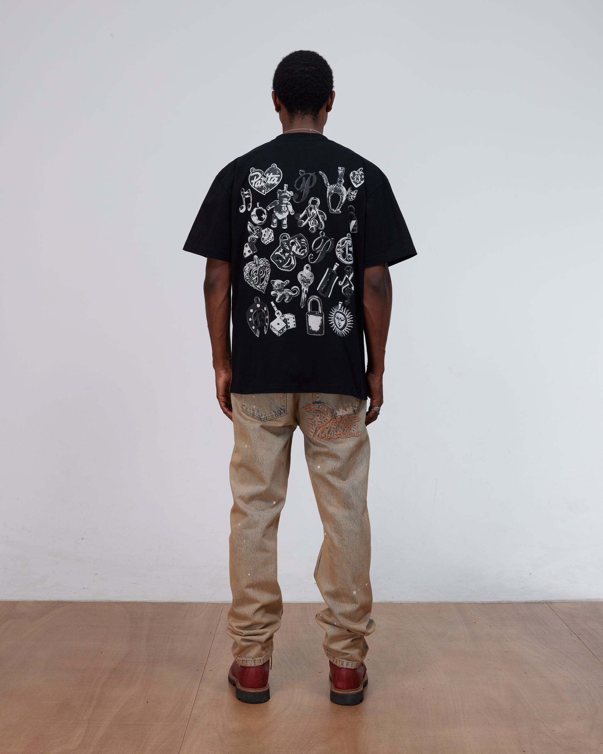 Back view of a model wearing the black Patta Charm T-Shirt with charms artwork.