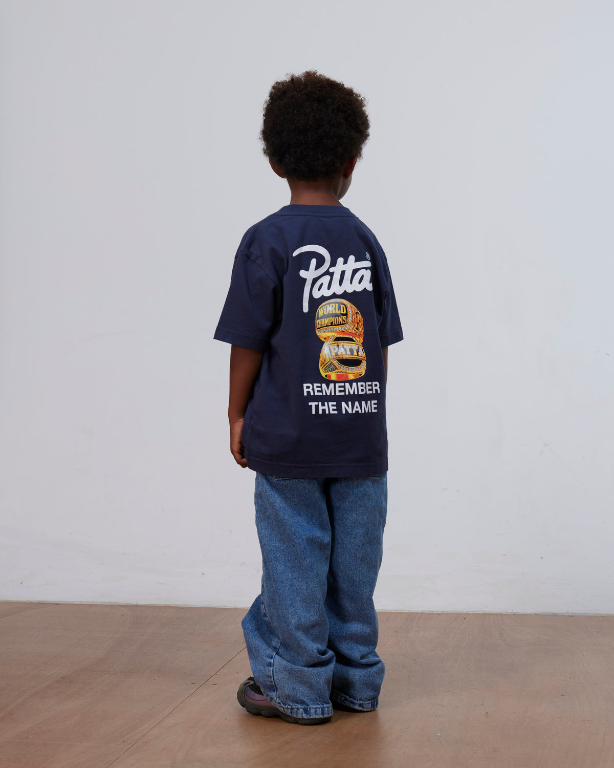 Back view of a child wearing the Patta Kids Championship T-Shirt in black iris with graphic print.