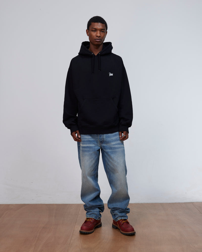 Front view of a model wearing the black Patta Kids Championship Hooded Sweater with blue jeans.